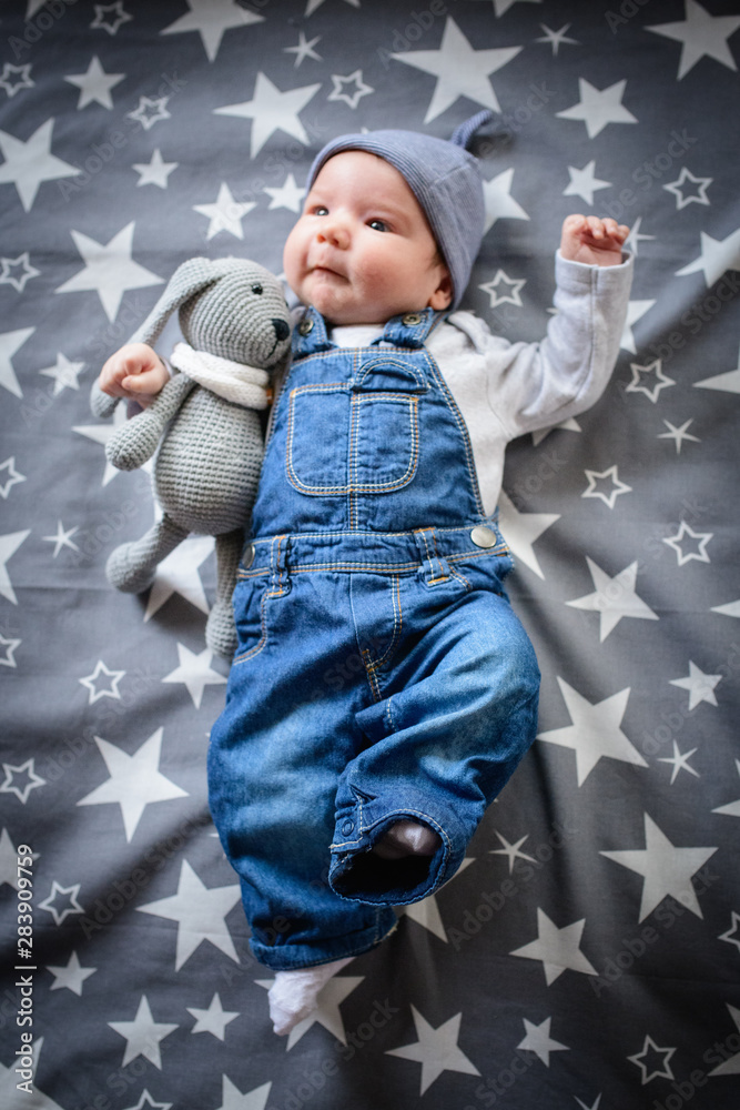 The child lies on a star blanket. Cute newborn baby girl lying in bed. Owl  child sleeping on a blue blanket with stars. in overalls from jeans. Top  view, flat lay Stock