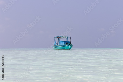 Ari Atoll, Maldives - 25 December 2018: A maldivian sailor is fishing on his blue boat called 'dhoni'