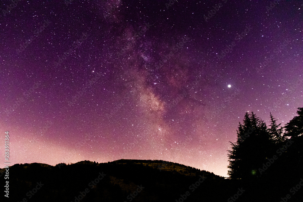 Beautiful purplish night landscape and scenery. Starry sky with milky way galaxy over the mountains and the cedar trees.