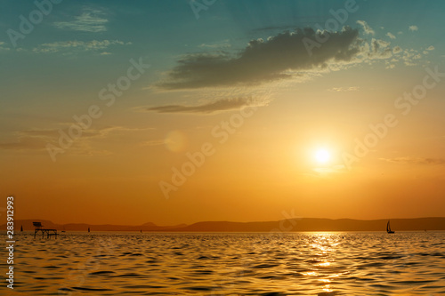 Beautiful sunset over lake Balaton with silhouettes of sailboat and angler pier in Hungary