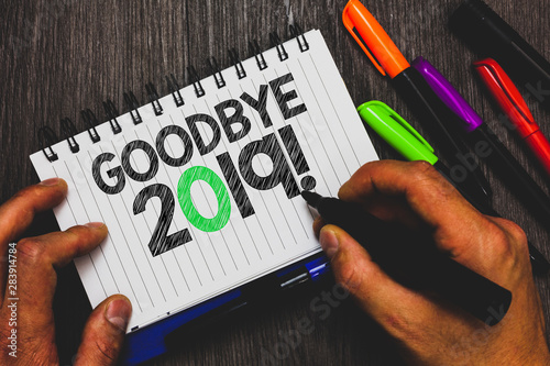 Handwriting text writing Goodbye 2019. Concept meaning New Year Eve Milestone Last Month Celebration Transition Man holding marker notebook paper communicating ideas Wooden background photo