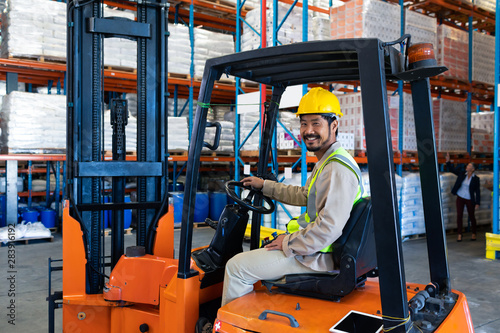 Male worker sitting in forklift and looking at camera in warehouse
