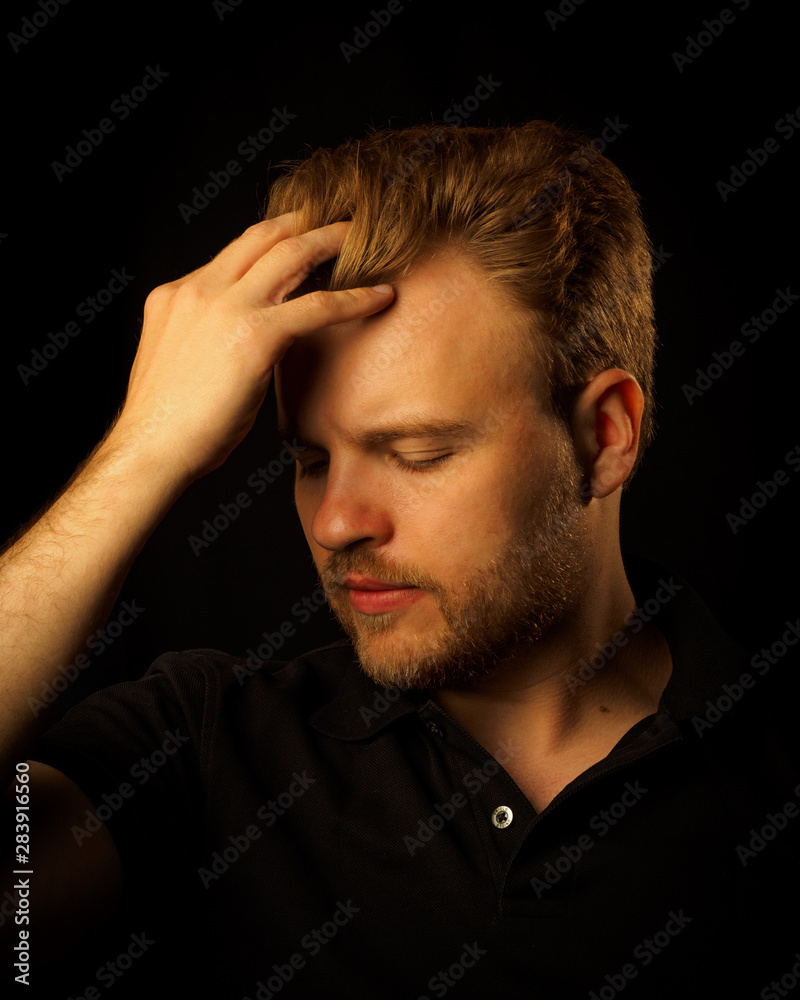 hipster young man with hand over hairstyle. the guy is sad and upset on a dark background.