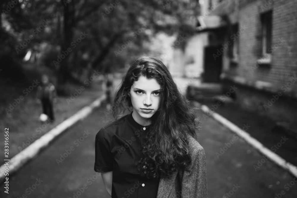 Young beautiful caucasian woman walking in old town. Black and white female art portrait. Stylish girl with long curly hair.