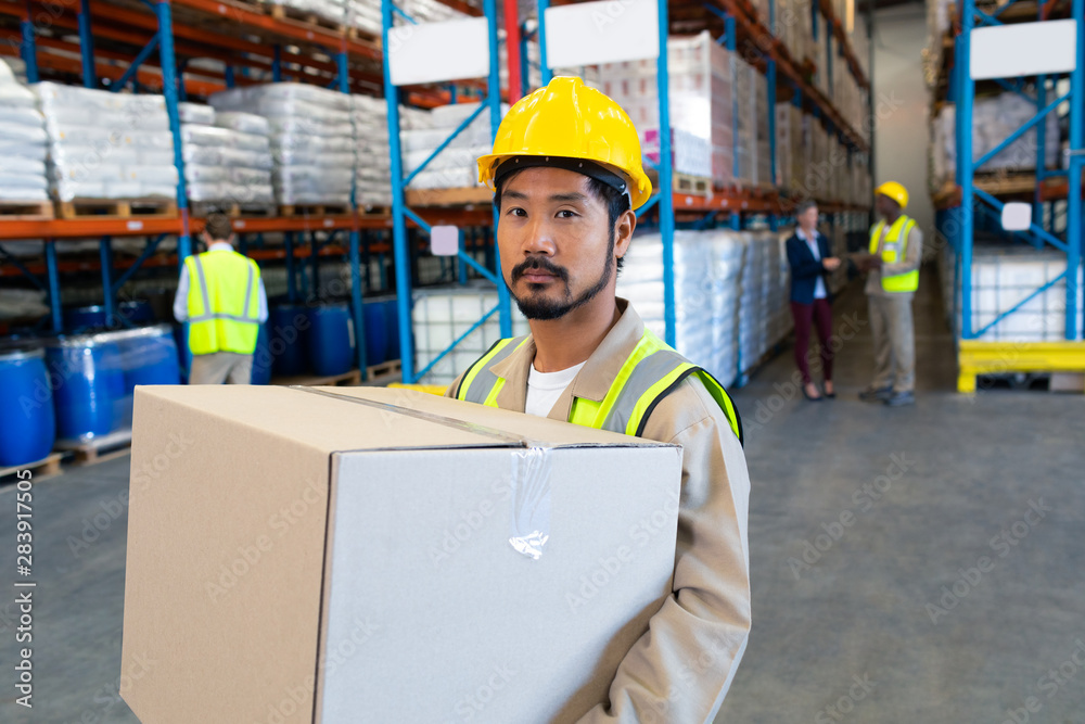 Male worker carrying cardboard box and looking at camera in warehouse Male worker carrying cardboard box and looking at camera in warehouse