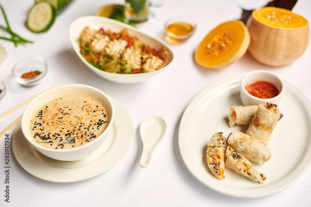 Above view of tasty dinner for one on white tablecloth. Oriental dinner from soup with seeds, tempura shrimps and noodles with vegetables preparing for client.