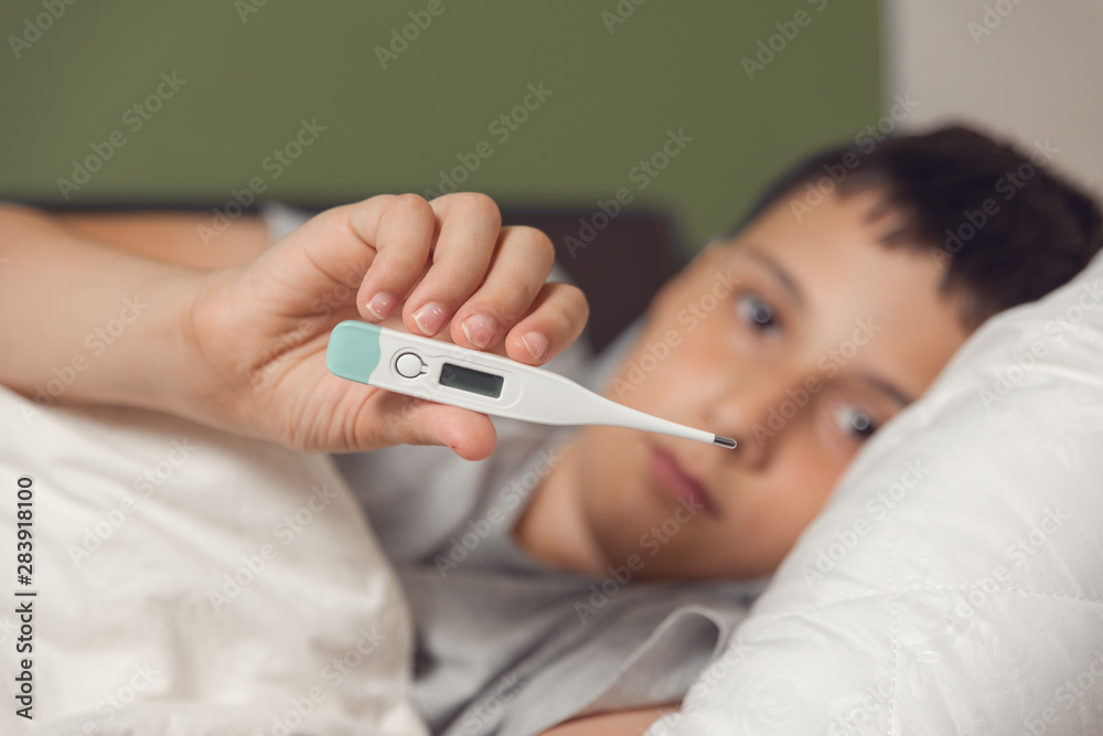 Sick boy with thermometer laying in bed. Sick child with fever and illness in bed. Flu. Cold Sick boy with thermometer laying in bed. Sick child with fever and illness in bed. Flu. Cold