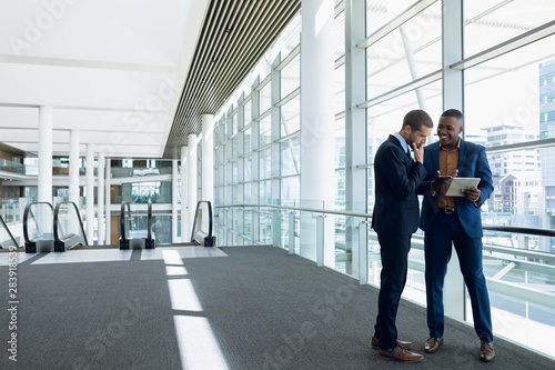 Two businessmen stand using tablet in office lobby photo