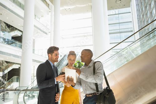 Diverse young business people with tablet talking in a modern atrium photo