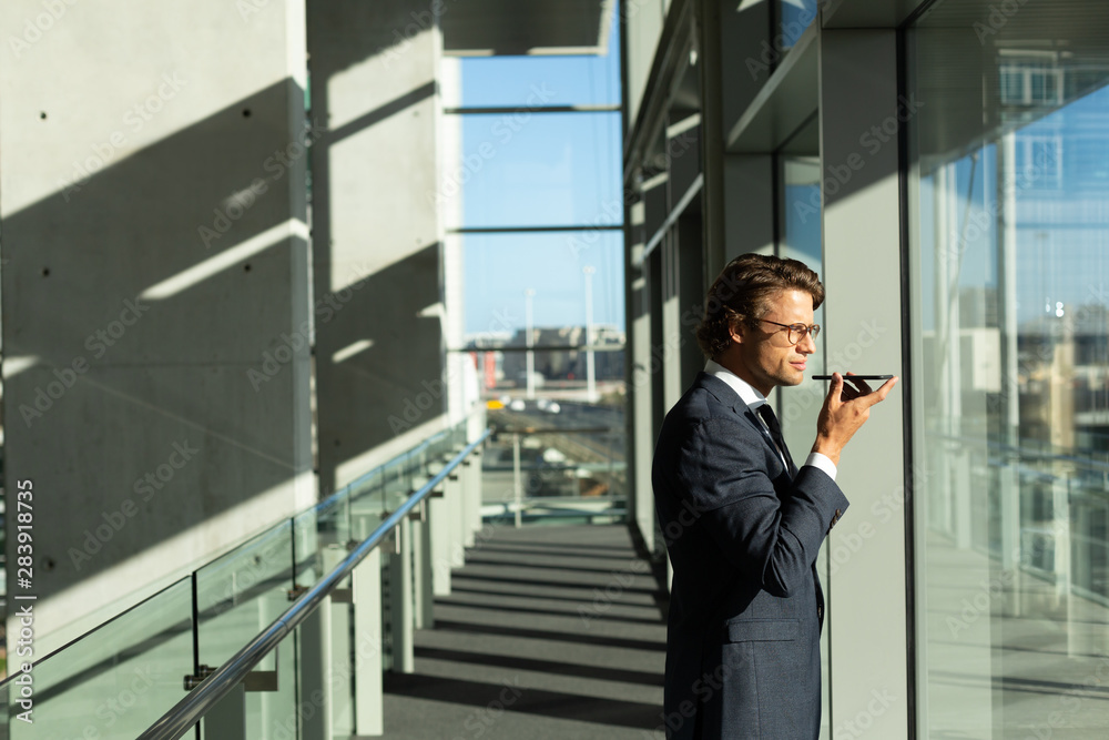 Businessman talking on mobile phone while looking through window in corridor at modern office