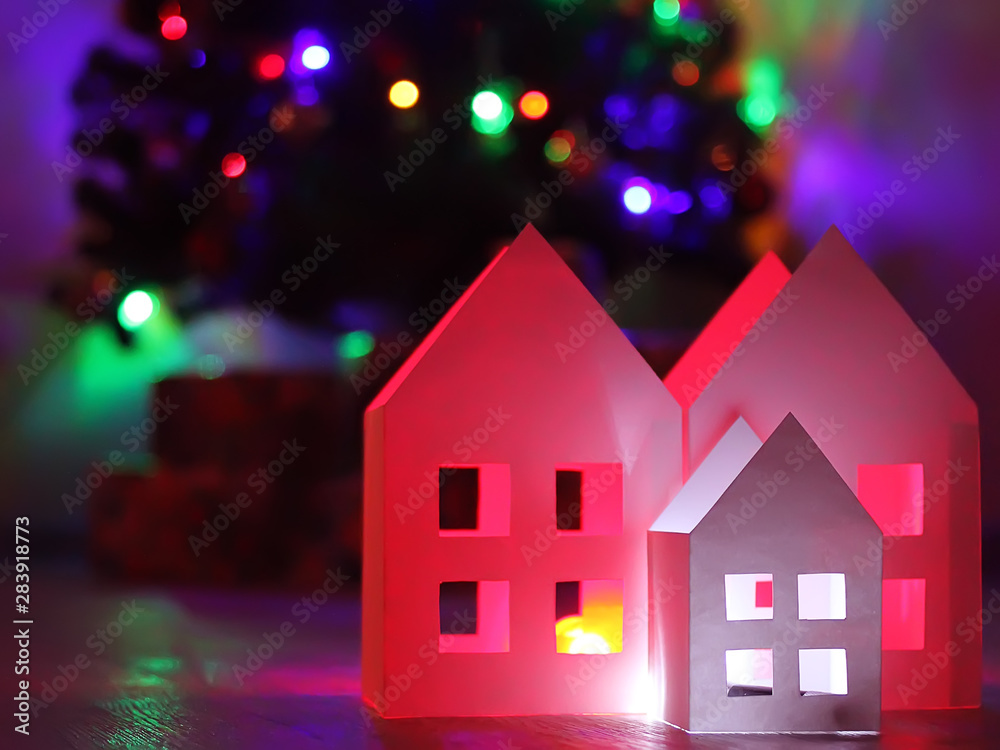 Houses made of paper against the backdrop of the New Year tree lights. Happy New Year and Christmas background Houses made of paper against the backdrop of the New Year tree lights. Happy New Year and Christmas background