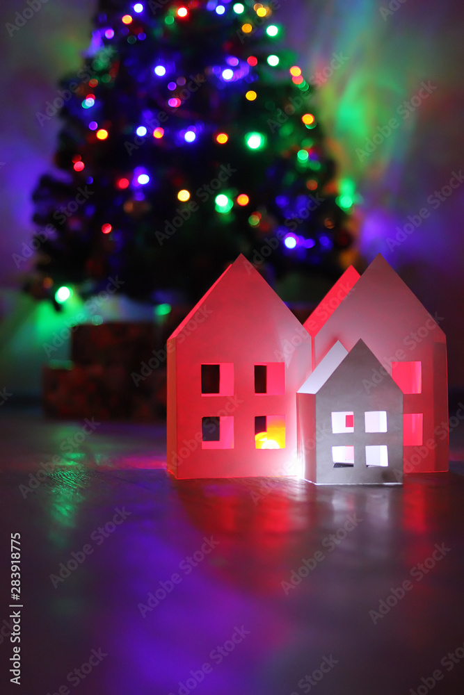 Houses made of paper against the backdrop of the New Year tree lights. Happy New Year and Christmas background Houses made of paper against the backdrop of the New Year tree lights. Happy New Year and Christmas background