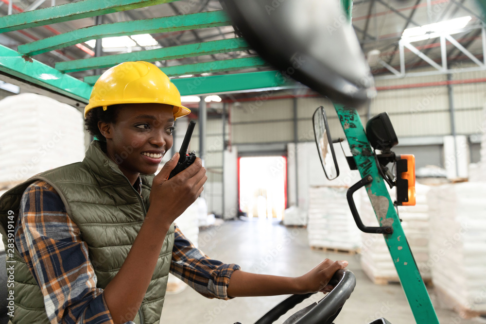 Female worker talking on walkie-talkie while driving forklift in warehouse Female worker talking on walkie-talkie while driving forklift in warehouse