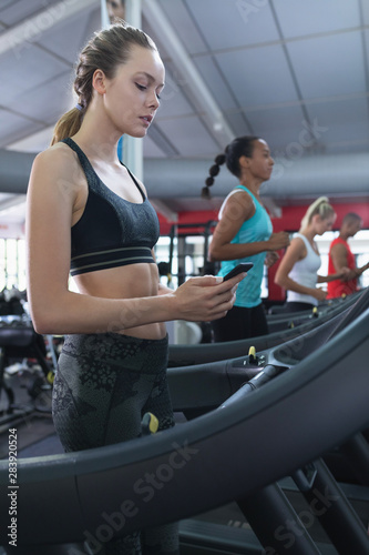 Woman using mobile phone while exercising on treadmill in fitness center