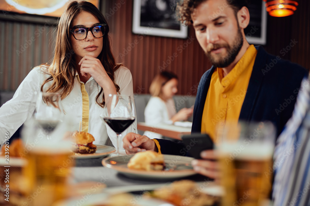 Young handsome Caucasian man having burgers for dinner while sitting in restaurant with his friends.