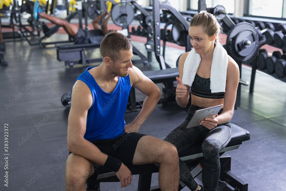 Fototapeta premium Female trainer and man interacting with each other while using digital tablet in fitness center