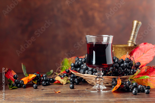 Fresh juice of ripe black chokeberry in glass and berries with leaves.