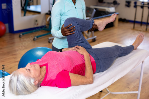 Physiotherapist stretching active senior woman leg in sports center 