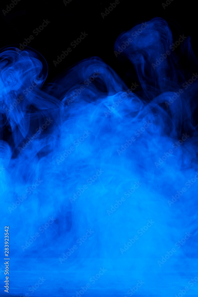 Conceptual image of blue smoke isolated on dark black background and wooden table.