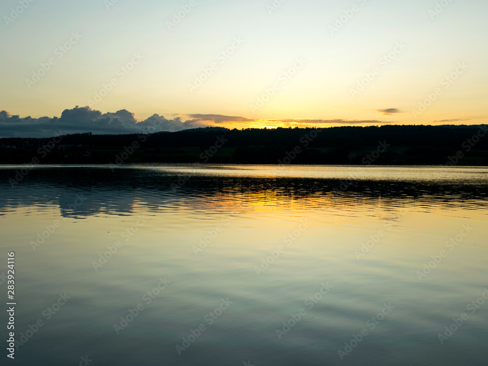 view of the lake at dawn early in the morning, silhouettes of hills and clouds