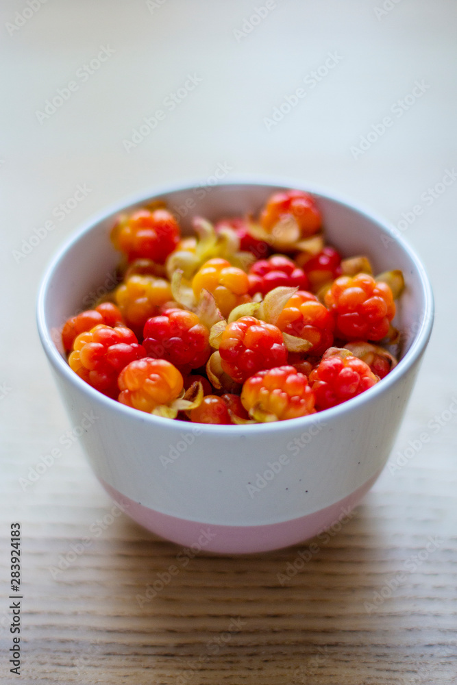 bright yellow-red cloudberries in a ceramic bowl on a wooden table, vertical frame bright yellow-red cloudberries in a ceramic bowl on a wooden table, vertical frame