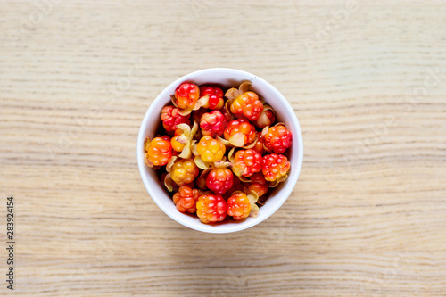 white ceramic round bowl with bright red-orange cloudberry on wooden table, top view