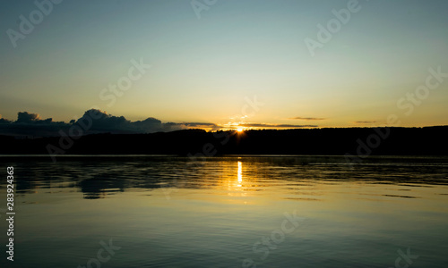 early morning on the lake, dusk, sun rising behind the hill