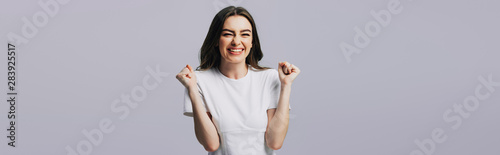 excited beautiful girl in white t-shirt showing yes gesture isolated on grey, panoramic shot