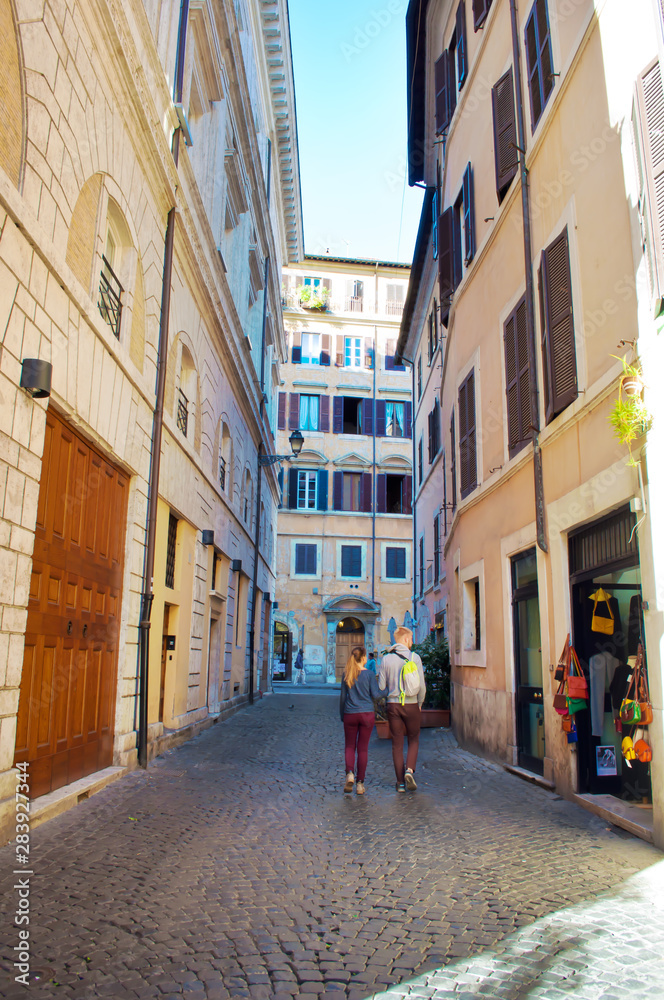 Young man and woman walking down a narrow solitary street in the city center of Rome