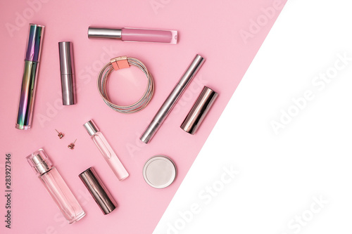 Flat lay composition with decorative makeup products and gold chain necklace on pastel pink background. Makeup and beaty concept. Copy space.
