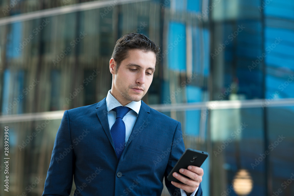 Serious young businessman in suit is texting message on phone in front of the glass bulding Serious young businessman in suit is texting message on phone in front of the glass bulding
