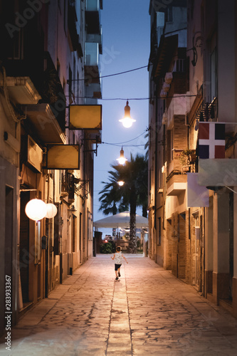 Little boy running down a narrow spanish street with lightbulbs  palm and blue evening skies on the background. Hope and travel concept.