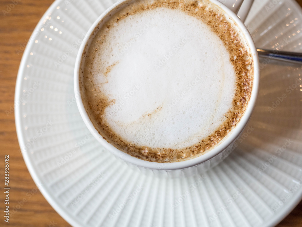 Hot coffee cappuccino latte isolated on timber table background in a cup and saucer with spoon