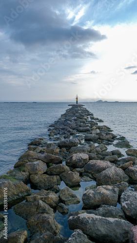 Lighthouse on a stone breakwater in the sea at sunset in cloudy weather in the summer. Summer evening. The concept of safe sea navigation. 