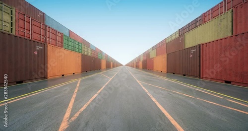 Endless rows of cargo shipping containers under blue sky. Camera moves slowly along stacked cargo containers painted in colors of different freight transportation business companies. Seamless loop.