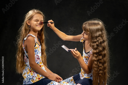 The girl closed her eyes when another girl powder her nose with a brush