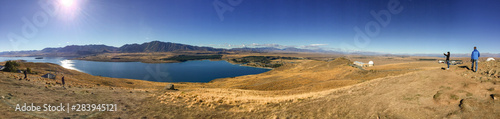 Sweeping panoramic views of the spectacular golden Mackenzie Basin from the top of Mt John including Lake Tekapo with people in the foreground