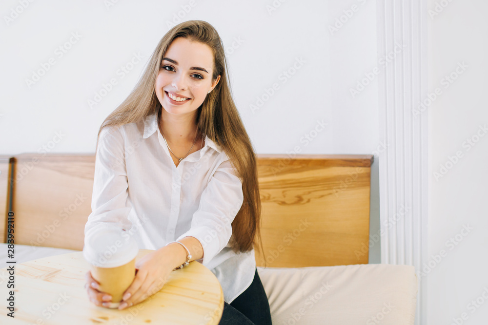 Happy smiling young woman with long hair sits at the table in a cafe with a cup of coffee. Happy smiling young woman with long hair sits at the table in a cafe with a cup of coffee.