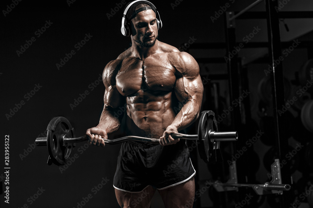 Muscular athletic bodybuilder fitness model training arms with barbell in gym. Concept sport photo of exercises in gym Muscular athletic bodybuilder fitness model training arms with barbell in gym. Concept sport photo of exercises in gym