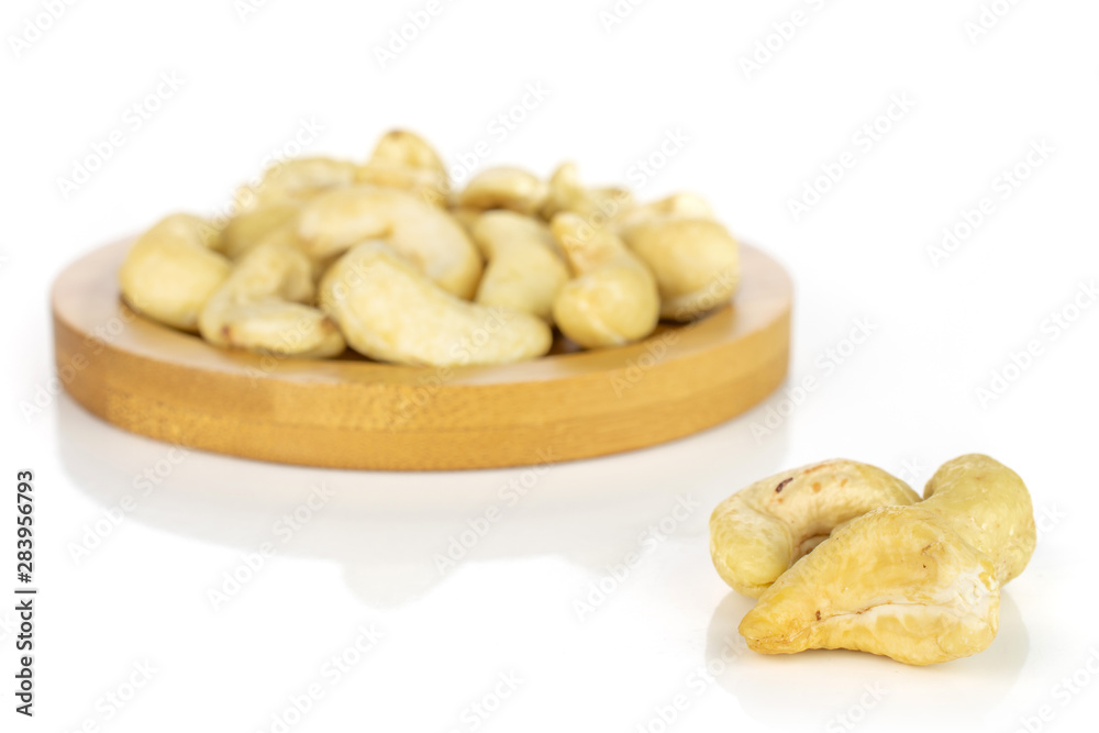 Fototapeta premium Lot of whole unsalted beige cashew on round bamboo coaster isolated on white background