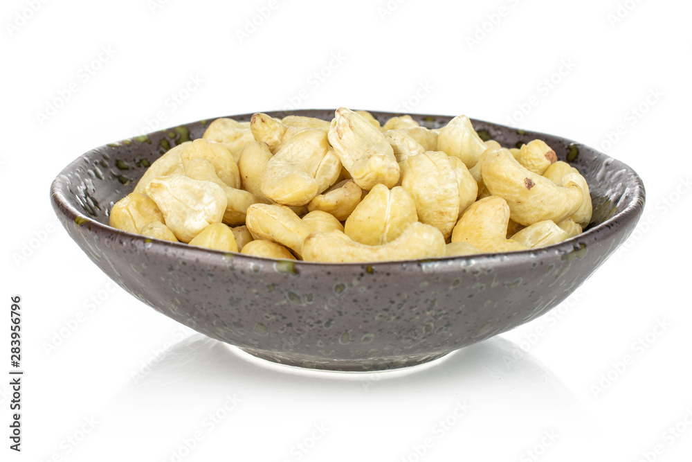 Lot of whole unsalted beige cashew in dark ceramic bowl isolated on white background Lot of whole unsalted beige cashew in dark ceramic bowl isolated on white background
