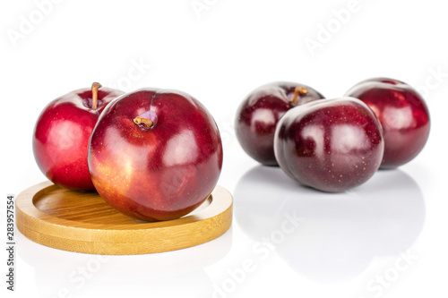 Group of five whole ripe red round plum on round bamboo coaster isolated on white background