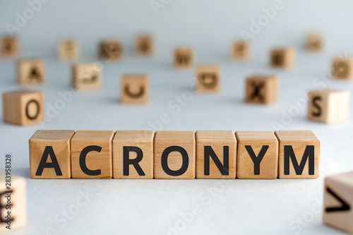acronym - word from wooden blocks with letters, use of acronyms in the modern world abbreviation concept, random letters around, top view on wooden background