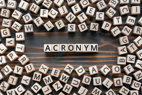 acronym - word from wooden blocks with letters, use of acronyms in the modern world abbreviation concept, random letters around, top view on wooden background photo