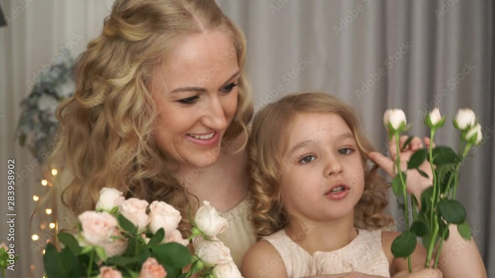 Close up of portrait of smiling mother with daughter sit at table with bouquet of pink roses and learn to count using flower buds Close up of portrait of smiling mother with daughter sit at table with bouquet of pink roses and learn to count using flower buds