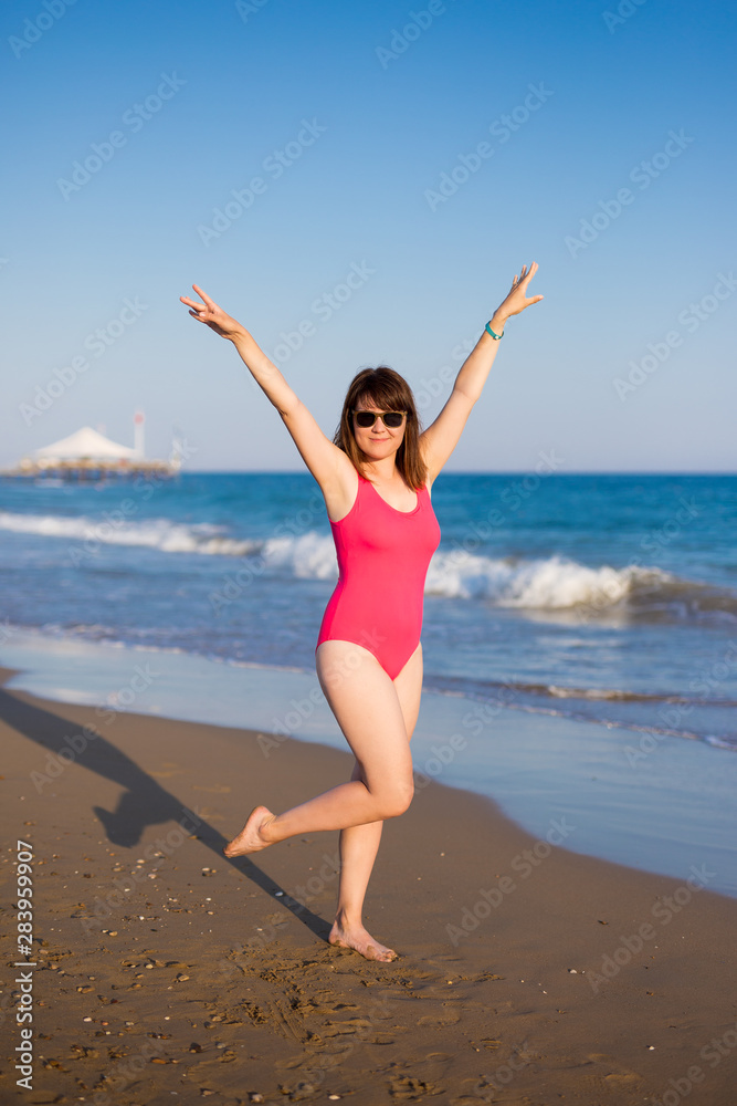 summer and travel concept - full length portrait of cheerful young beautiful woman in pink swimsuit at the beach summer and travel concept - full length portrait of cheerful young beautiful woman in pink swimsuit at the beach