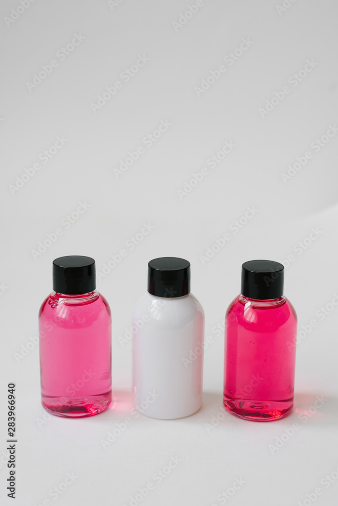 Mini bottles of pink and white color with body care cosmetics or hair on white background. Improvement of the hotel. Copy space