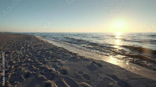 Sun low above horizon, sandy beach of Baltic sea at Curonian spit, soft waves