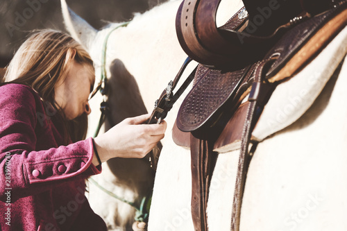 Western horseback riding concept shows preparation of woman putting saddle on horse to ride close up.