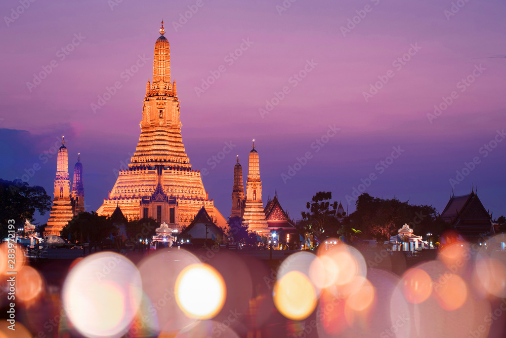 Naklejka premium Świątynia Wat Arun z zachodem słońca i rozmycie bokeh na pierwszym planie podczas zachodu słońca.